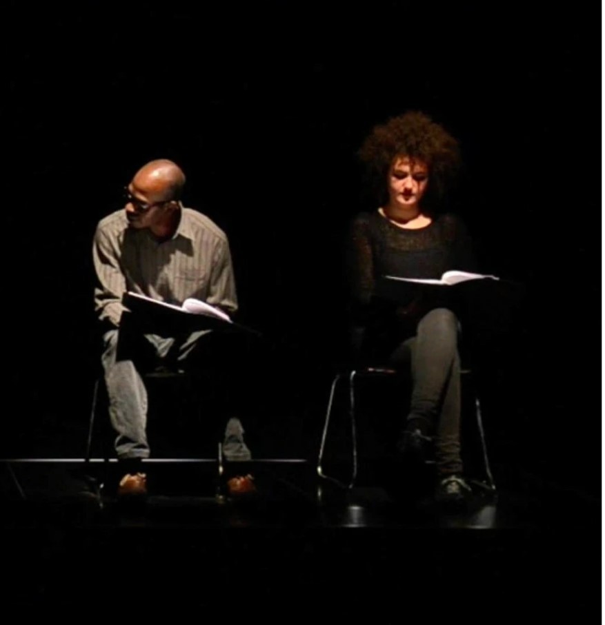 two persons seating on a stage with a black background