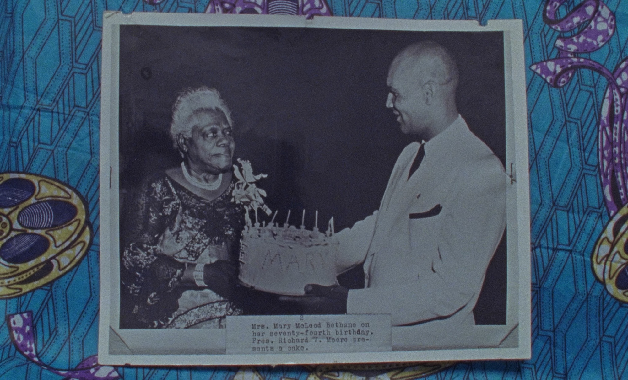 An archive black and white photo with a man presenting a birthday cake to an elderly woman. The text on the photo reads: Mrs. Mary MoLood Bethune on her seventy-fourth birthday. Press. Richard. Mooro pre sent a cake.