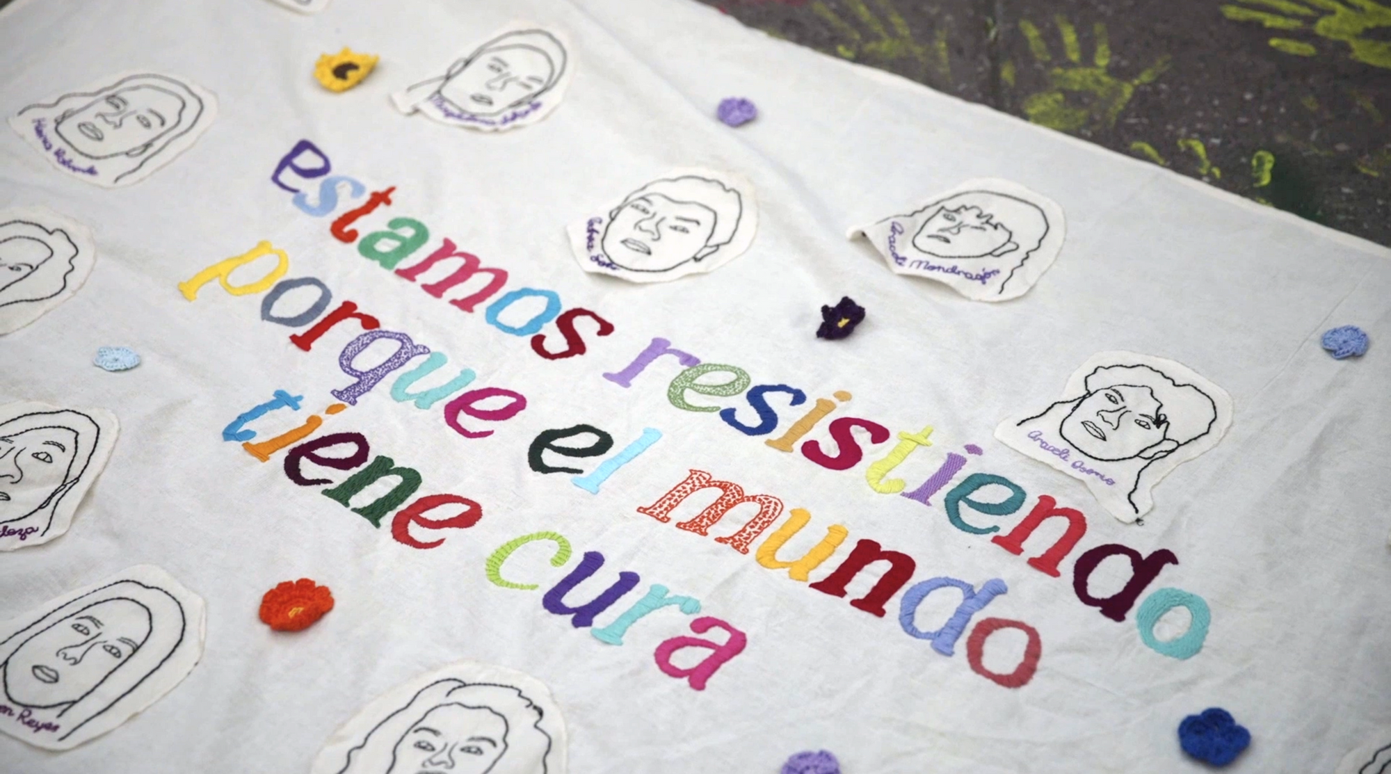A protest banner with colorful text that reads "estamos resistiendo porque el mundo tiene cura" with faces.